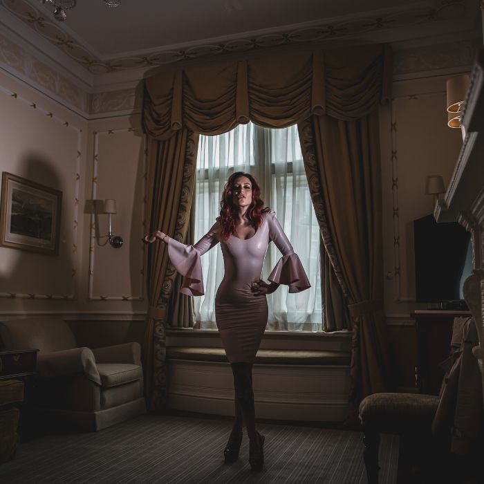 Mistress Adreena standing in a luxurious room.
