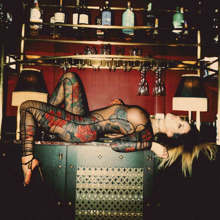 Mistress Adreena in a mesh outfit, layed across a bar.