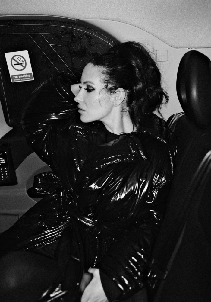 Adreena in a taxi cab on her way to your place, dressed in a hot black jacket with sleek hair.