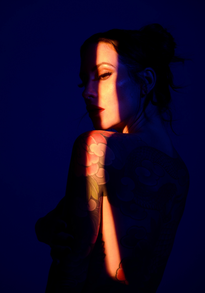 Adreena in a dark blue room, lit with a sliver of golden warm light.