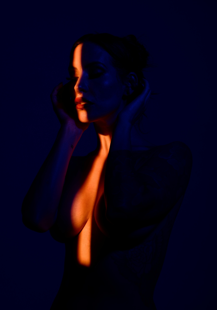 Adreena in a dark blue room, lit with a sliver of golden warm light.